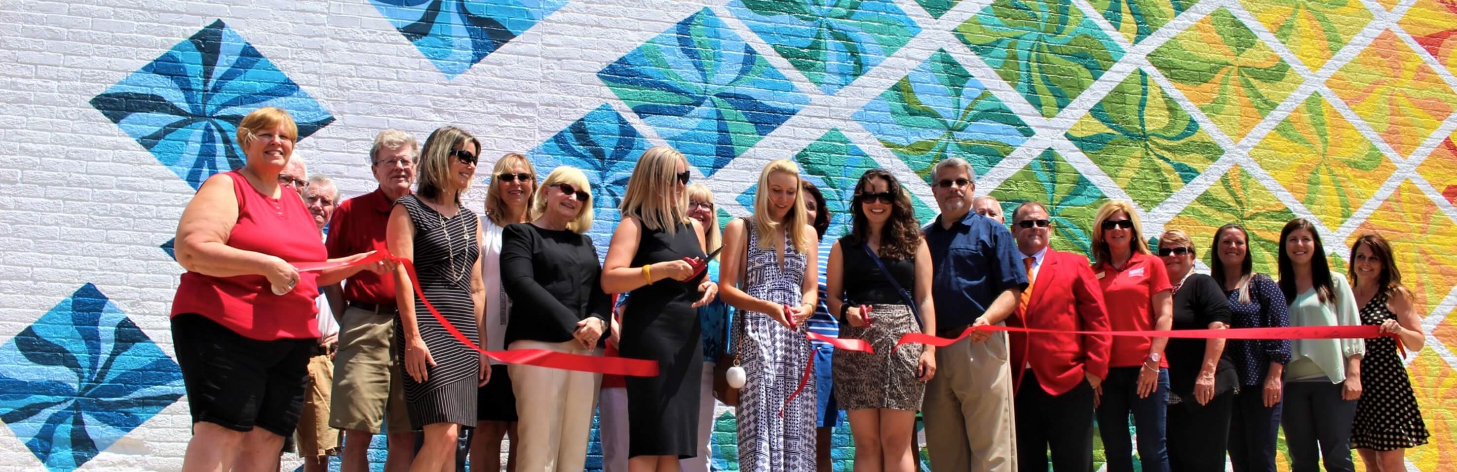 Group cutting ribbon in front of large mural painting