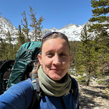 White woman in blue shirt in front of forest background