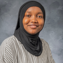 Black woman in black hijab in front of marbled grey background