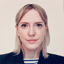 White woman with blond hair stands in front of muted beige background