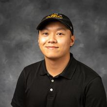 Asian man with black hat on in front of marbled grey background