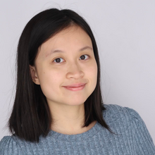 Asian woman with light blue sweater in front of grey background